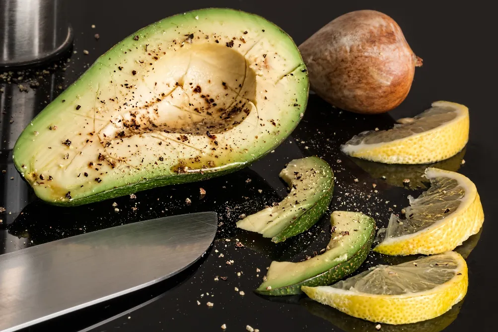 A black surface showcases avocados, emphasizing their role as sources of healthy fats.