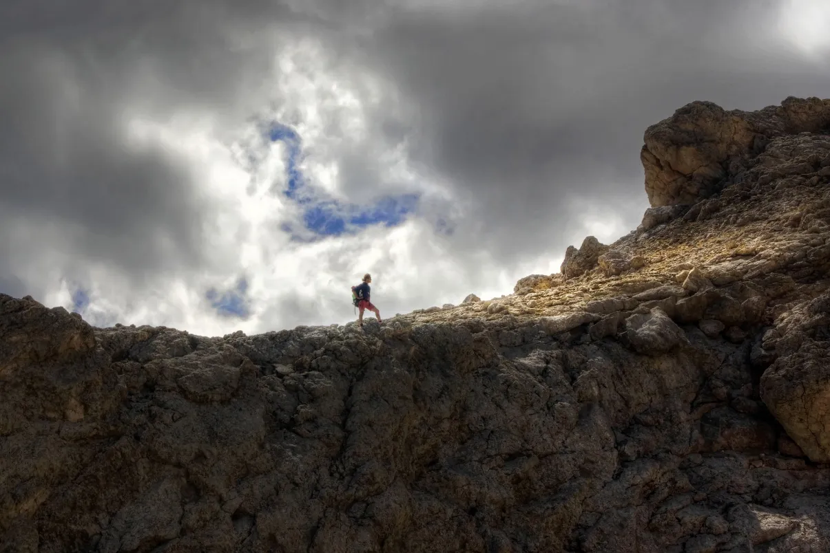 A man stands atop a mountain, ready for any challenge that may come his way.