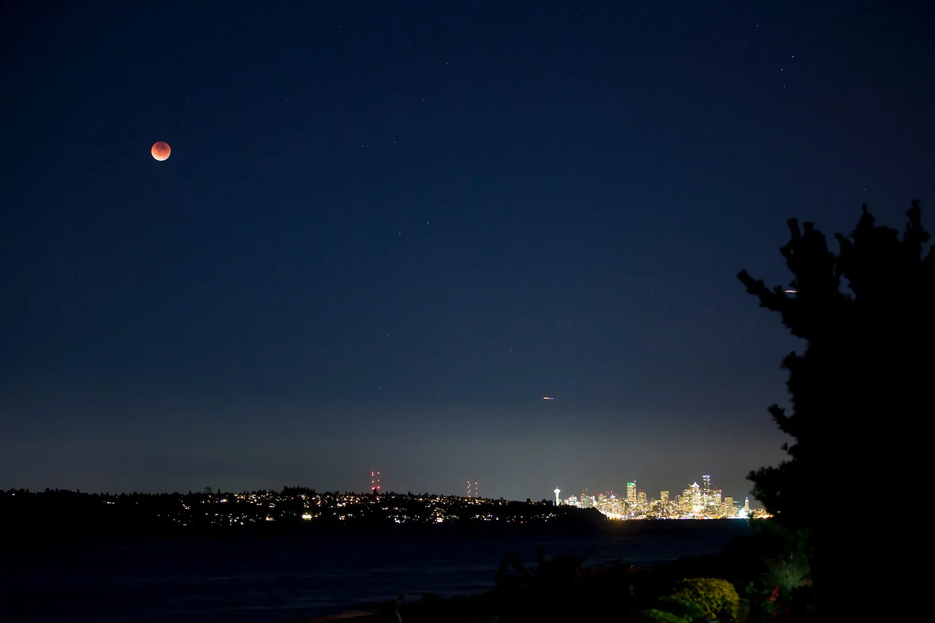 The image shows a group of people watching a lunar eclipse over a city skyline.