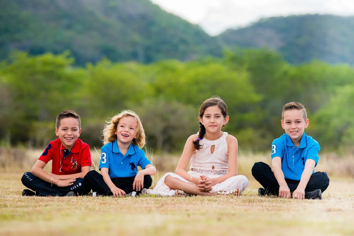 Four young children sitting on the green grass in a vast field, enjoying the serene surroundings.
