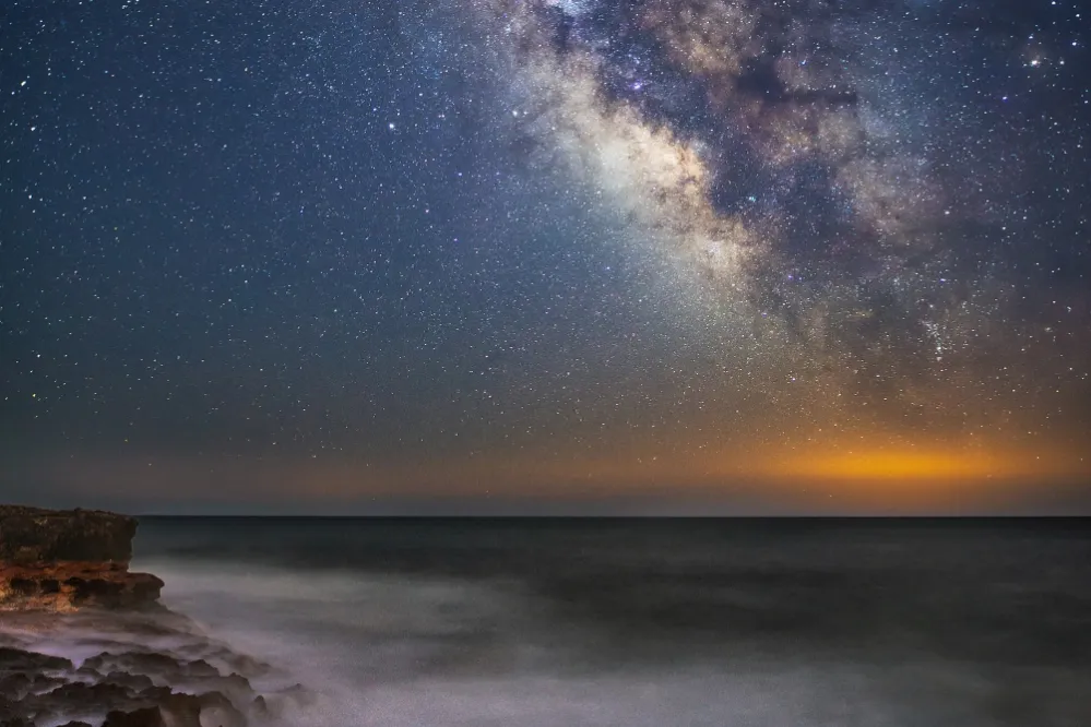 A stunning view of the Milky Way galaxy shining brightly over the dark ocean waters at night.