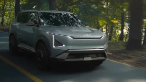 A Kia EV5 driving down a road next to a forest.