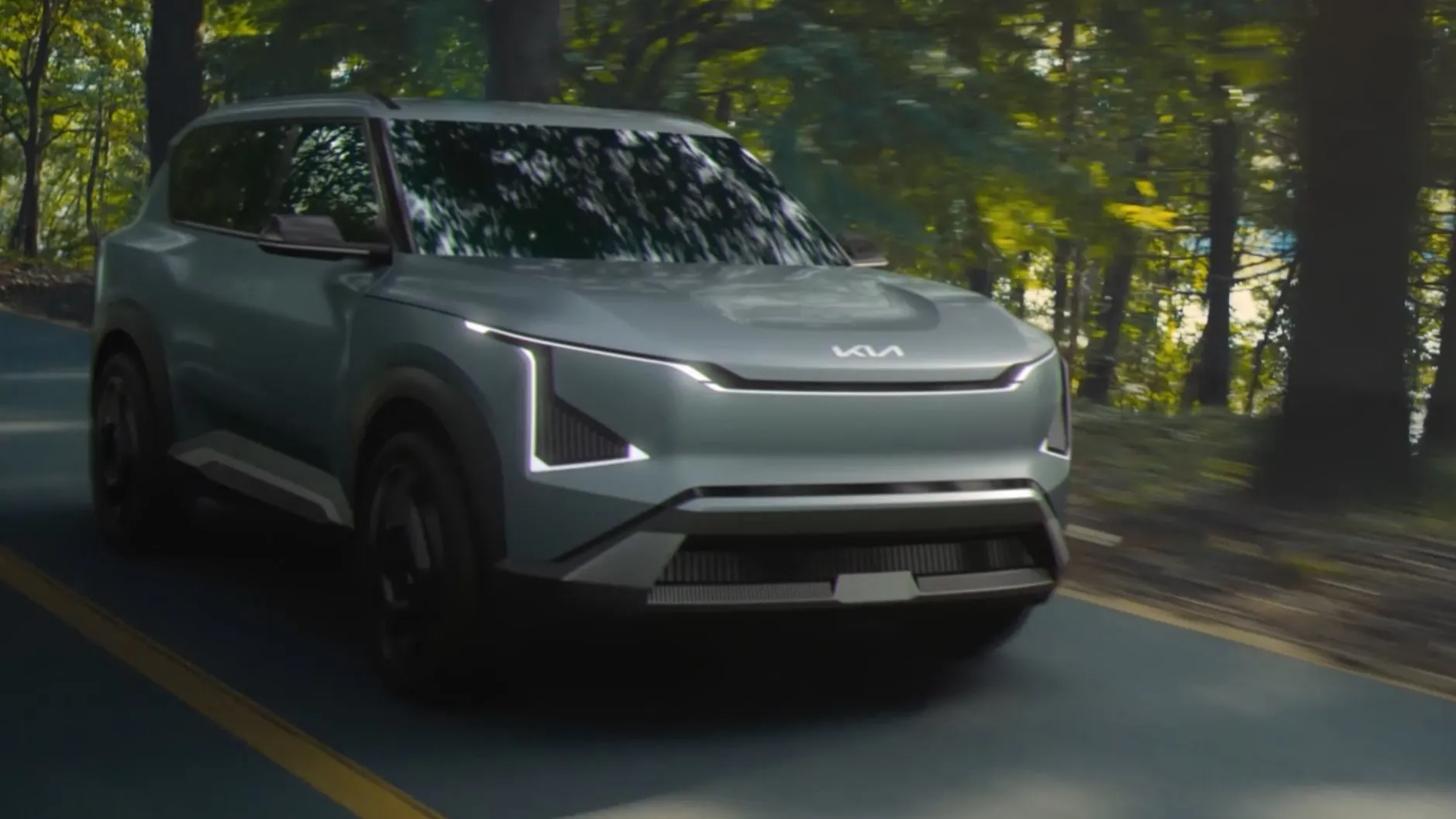 A Kia EV5 driving down a road next to a forest.
