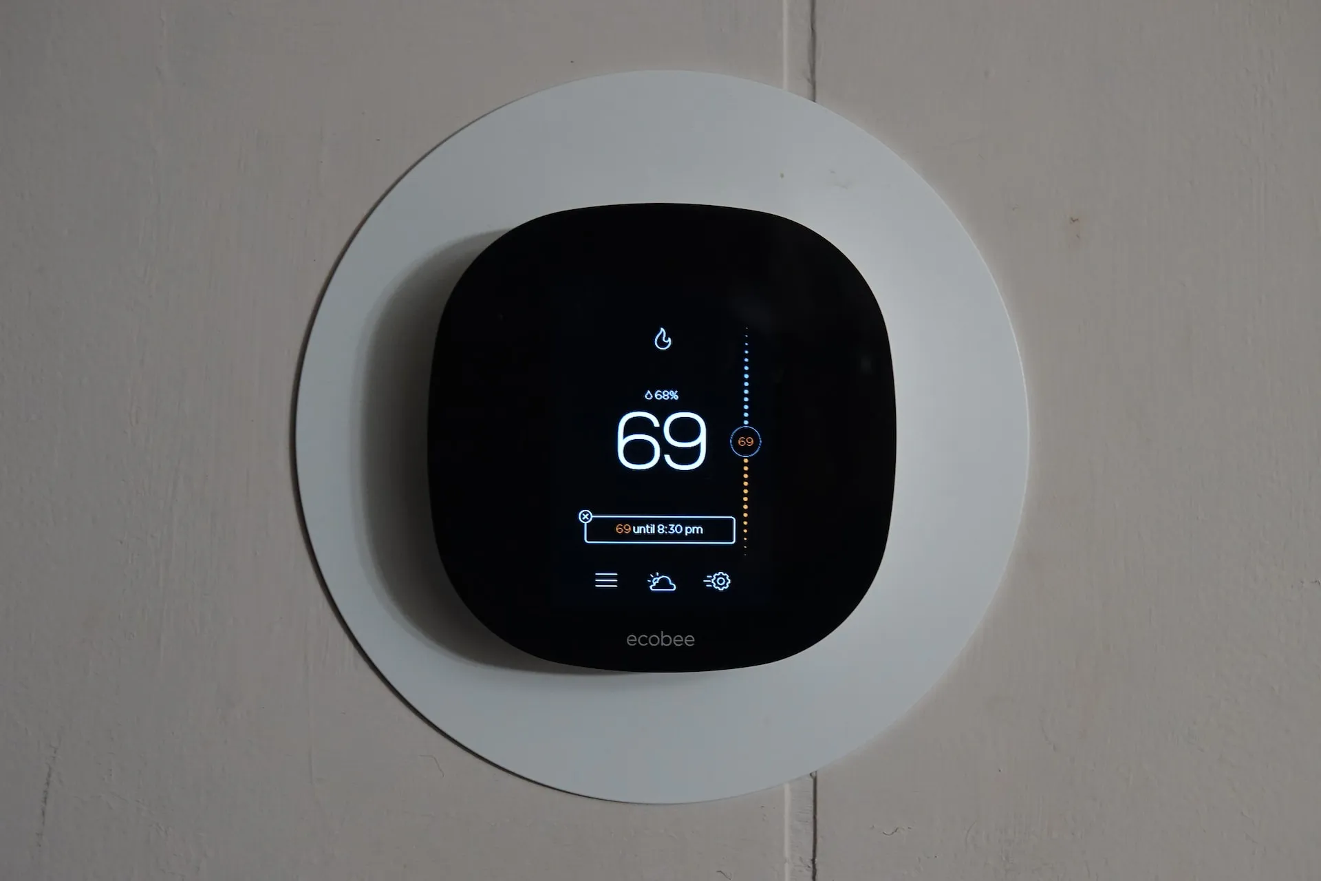 A smart thermostat mounted on the wall, depicted in the image, requires alt text that is concise and limited to 125 characters or less.