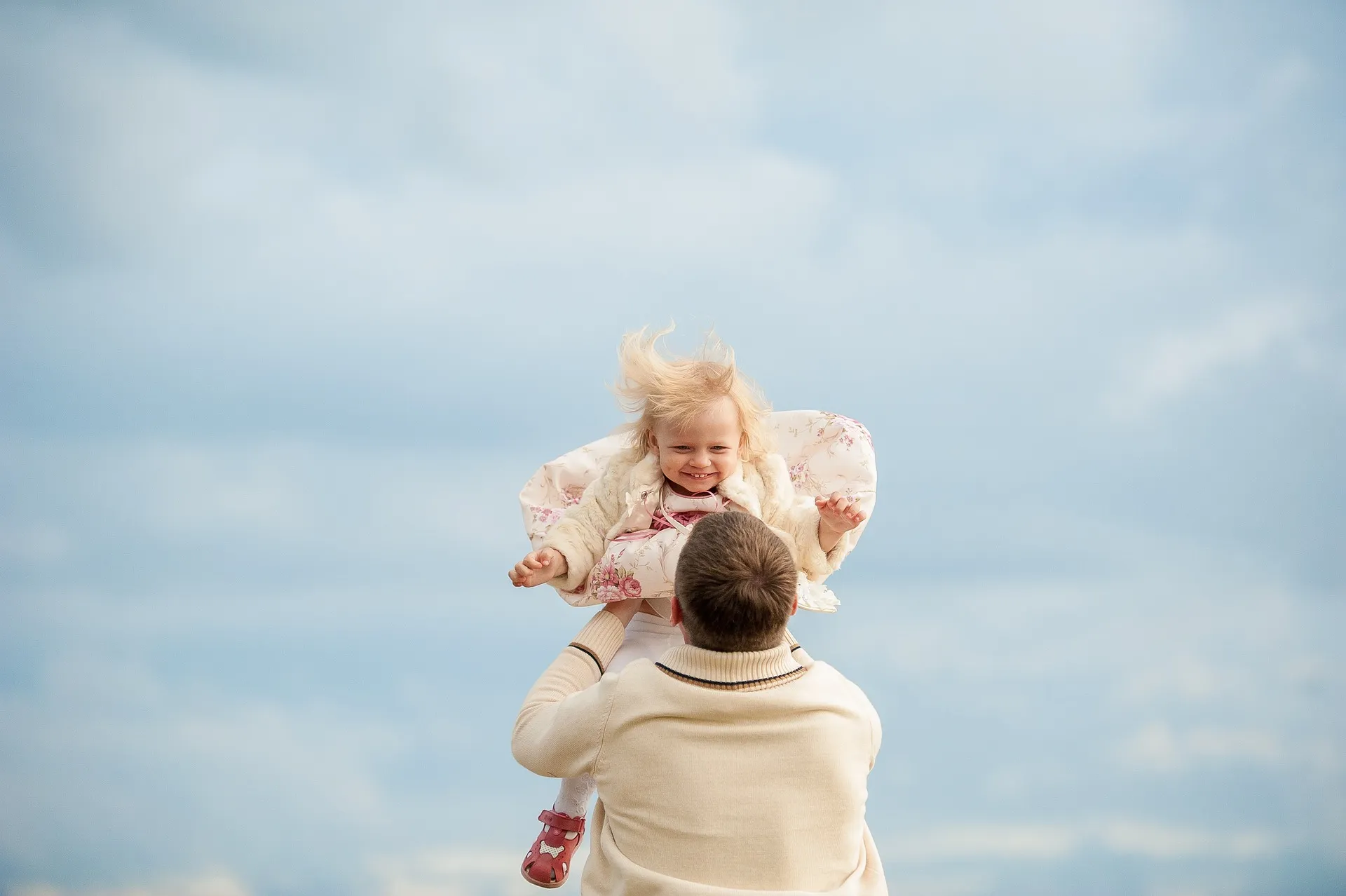 An adult male playfully raises a small girl into the air, showcasing their shared happiness.