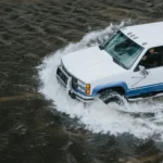 A white truck cautiously traversing flooded terrain amidst natural disaster warning signs and scientific explanation.