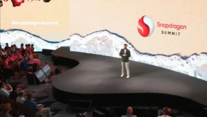 A man stands on a stage in front of a crowd at the Snapdragon Summit 2023.