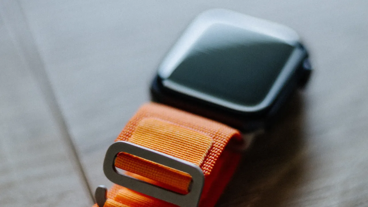 Apple watch strap featuring a sleek design with a vibrant orange buckle.