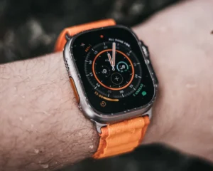A person wearing an Apple Watch with an orange strap on their wrist, displaying the time and other features.
