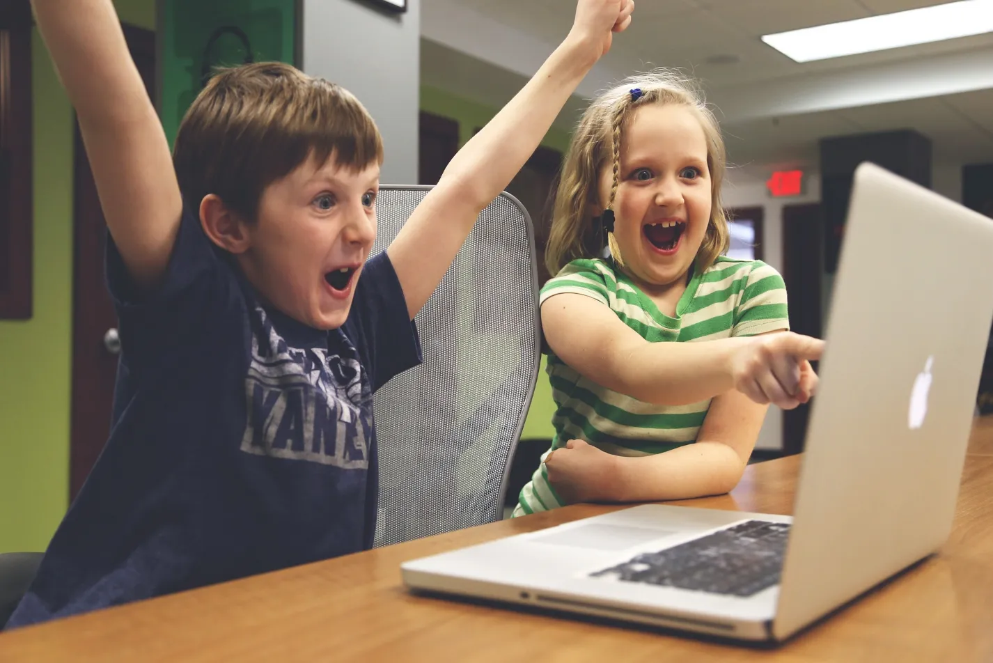 Two children, one boy and one girl, sit attentively in front of a laptop computer, utilizing the advantages of technology.