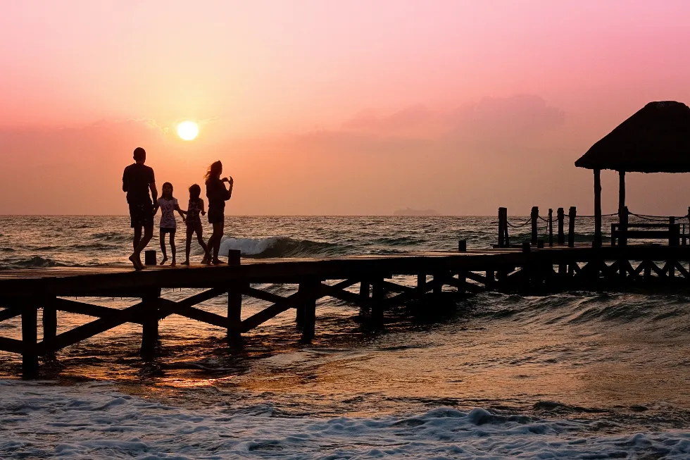 A family of four, silhouetted against a vibrant sunset, stands together on a serene pier.