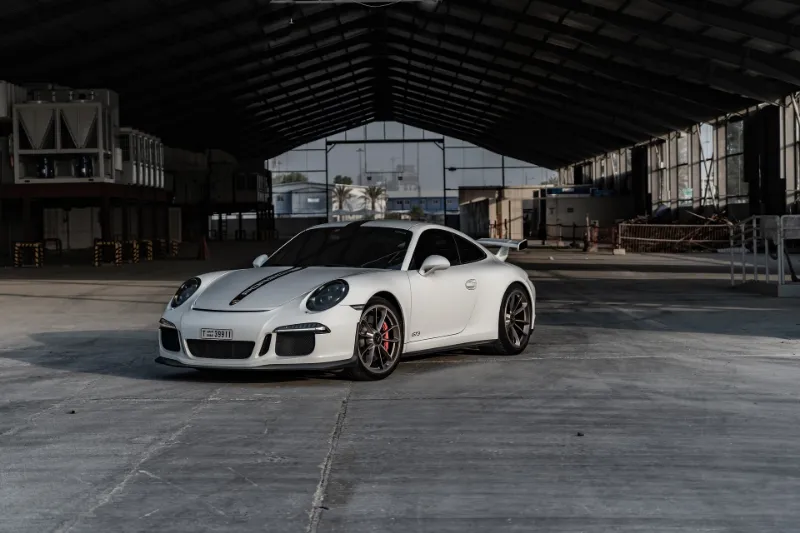 A white Porsche 911 GTS parked in an empty warehouse, showcasing its sleek design and elegance.