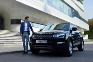 A well-dressed man standing beside a black Land Rover, exuding elegance and sophistication.