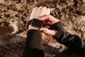 A person wearing a black jacket and holding a sports smartwatch.